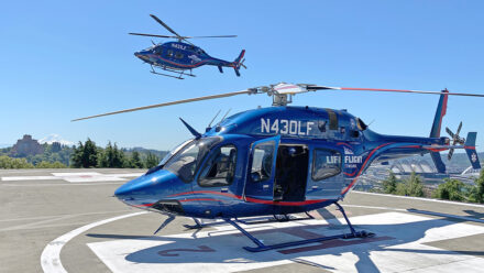 Life Flight Network helicopter is seen on landing pad with another airborne helicopter taking off in background