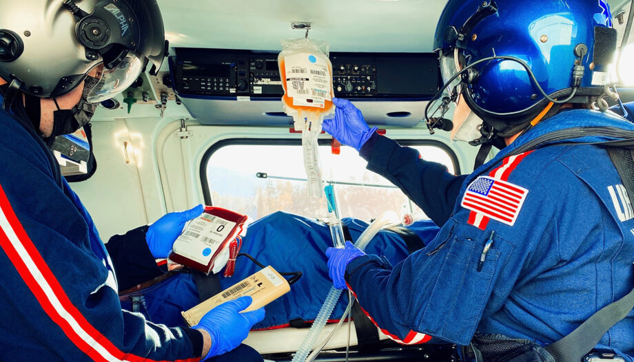 Two flight nurses hold an IV bag of plasma in the air, while another holds a bag of blood. They tend to a patient during a flight