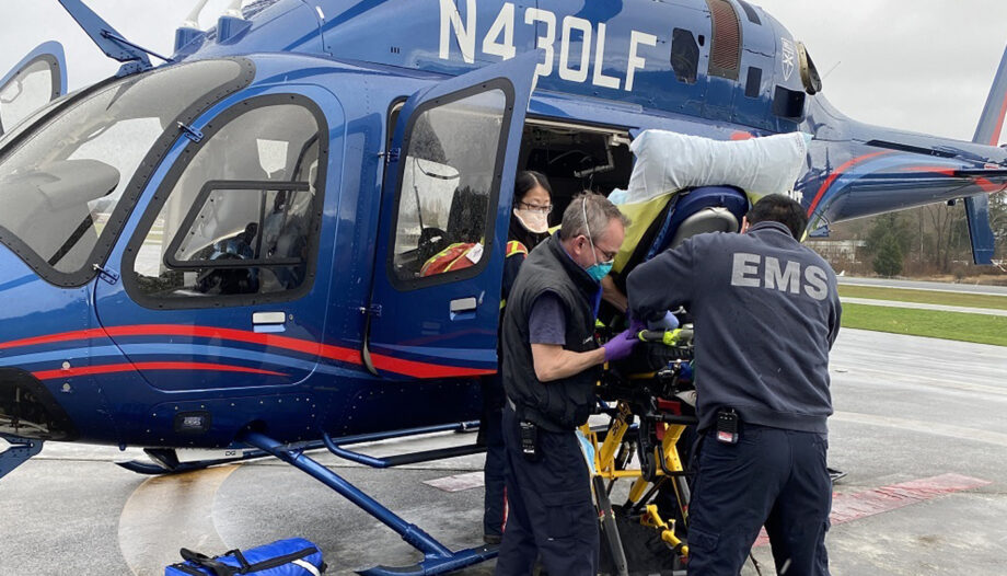 Flight crew and an EMS agent load a patient into a waiting helicopter