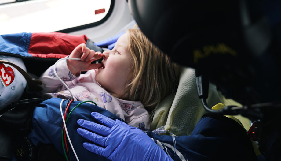 Close up of young girl patient with probes for vitals sucks her thumb as a nurse comforts her.