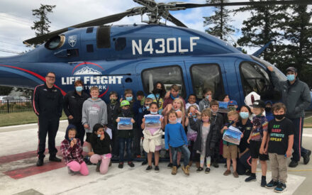 A group of younger kids poses in front of a helicopter holding certificates. Life flight crew flank them.