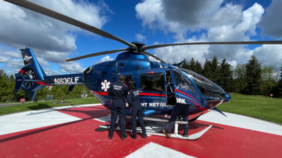 Three crew stand near helicopter on a landing pad