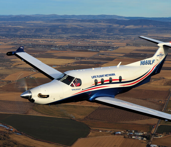 Single-engine prop plane is shown mid flight with high desert landscape seen below