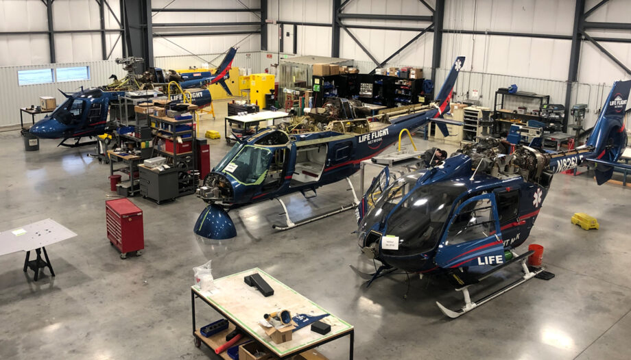 Wide angle view from above of three helicopters partially disassembled and undergoing maintenance