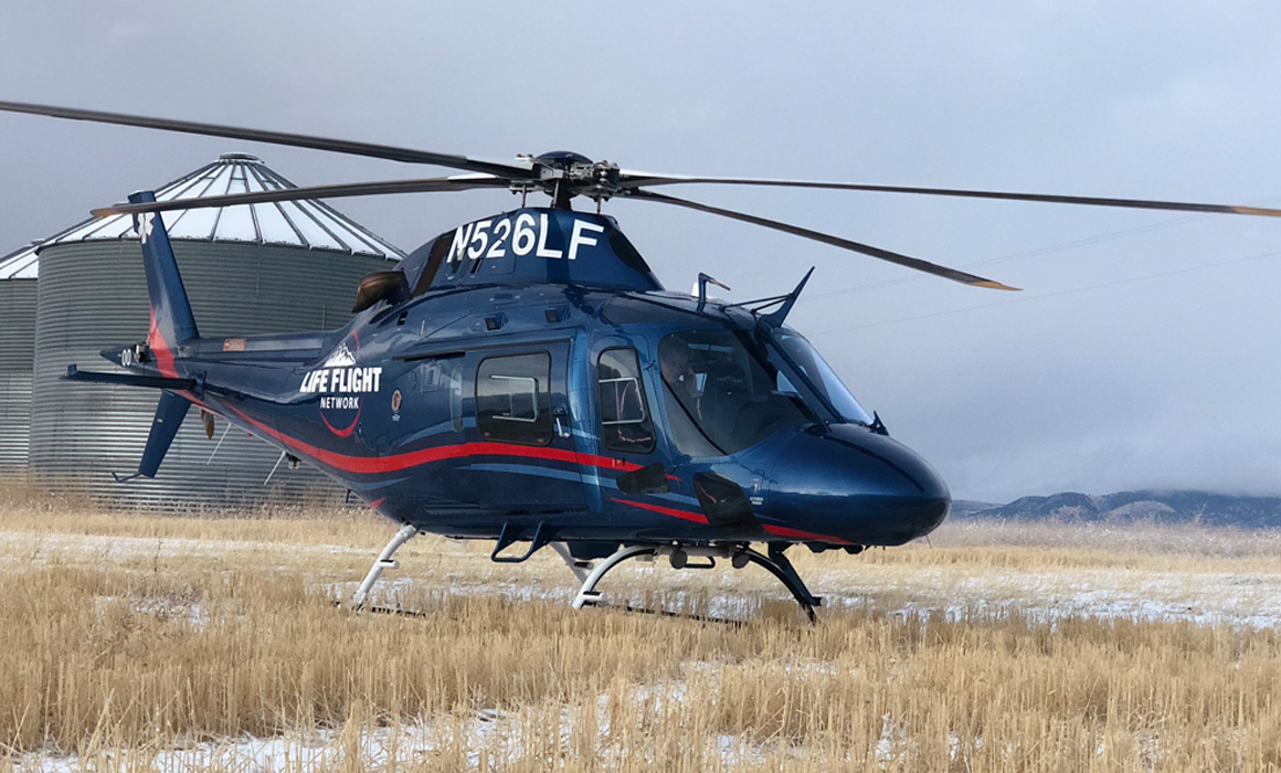 AW119KX "KOALA” sits in remote location with short brown grass and a dusting a snow. A barn silo is in the background.