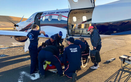 A crew of EMS and flight nurses prepare to lift patient on gurney into a fixed-wing propeller airplane