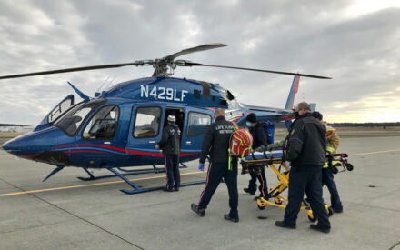 A flight nurse and two EMS technicians wheel patient to waiting helicopter with crew waiting to receive