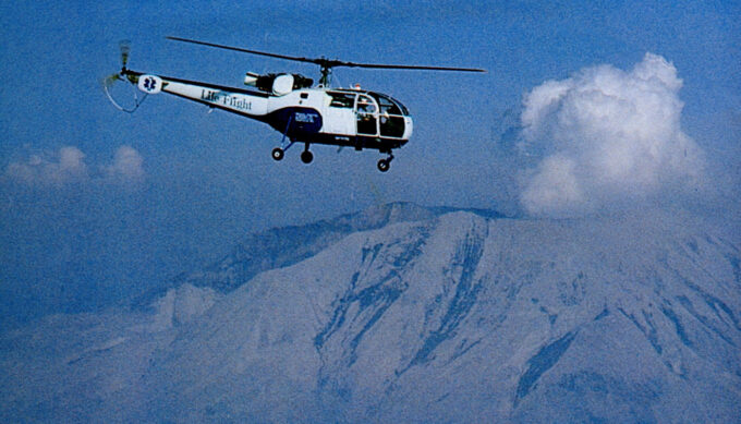 Historical photo from the '70s. Blue and white helicopter with retro-looking Life Flight logo flying above Mt. St. Helens