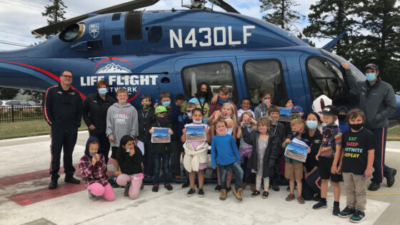 A group of younger kids poses in front of a helicopter holding certificates. Life flight crew flank them.